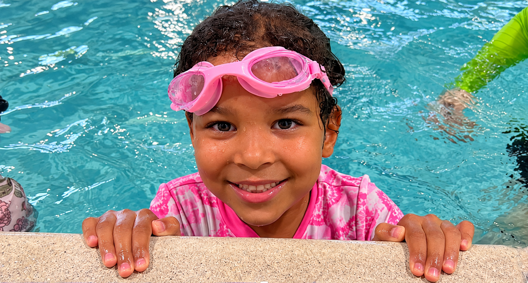 Young swimmer wearing pink goggles at the pool edge